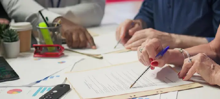 Three people at a desk review printed documents and charts with pens, the kind of paperwork a medical claim audit checks for coding and billing compliance.