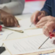 Three people at a desk review printed documents and charts with pens, the kind of paperwork a medical claim audit checks for coding and billing compliance.