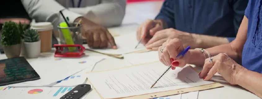 Three people at a desk review printed documents and charts with pens, the kind of paperwork a medical claim audit checks for coding and billing compliance.